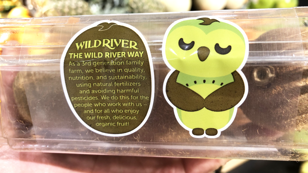 Our Owl Friends and associated kiwi owl logos are trademarks of Wild River Marketing Inc. Designed by Ben Young Landis and Guy Rogers. The photo shows the back side of a Wild River plastic clamshell container for kiwifruit. Next to a green kiwi owl, the text reads: The Wild River Way: As a third generation family farm, we believe in quality, nutrition, and sustainability, using natural fertilizers and avoiding harmful pesticides. We do this for the people who work with us — and for all who enjoy our fresh, delicious, organic fruit!